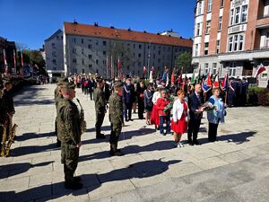 mundurowi ustawieni na placu pośrodku osoby z kwiatami ustawione w rzędzie