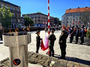 trzy kobiety w strojach moro zaciągają na maszt flagę państwową