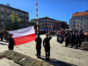 trzy kobiety w strojach moro, dwie trzymają flagę państwową, jedna salutuje