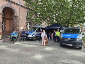 dwa radiowozy policyjne, motocykl i stoisko policjantów przed budynkiem sądu