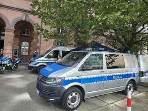 dwa radiowozy policyjne, motocykl i stoisko policjantów