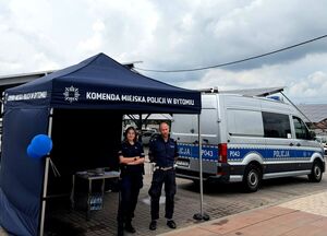 stoisko bytomskich policjantów przy nim policjant i policjantka, obok radiowóz