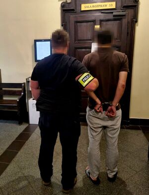 nieumundurowany policjant trzyma zatrzymanego mężczyznę w kajdankach przed salą