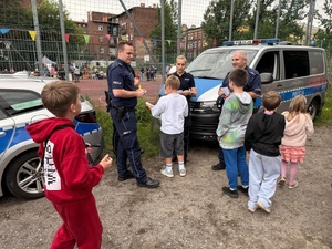 policjanci przy radiowozach służbowych, obok nich dzieci