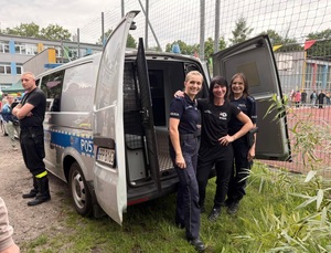 dwie policjantki pomiędzy nimi dziewczyna stoją przy radiowozie obok strażak