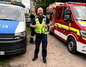 policjant ruchu drogowego stojący między radiowozem policyjnym i wozem strażackim