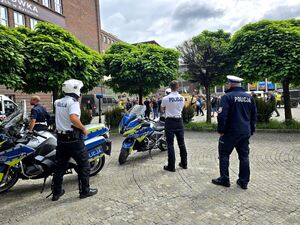 czterech policjantów przy motocyklach służbowych obserwują bawiące się osoby na zlocie