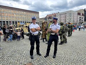 dwóch policjantów ruchu drogowego stoją pośród uczestników zlotu pojazdów militarnych