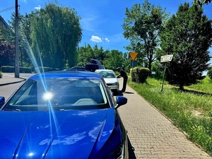 pojazdy zaparkowane przy jezdni, przy jednym z nich policjant