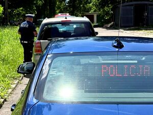 nieoznakowany radiowóz w nim wyświetlony napis Policja, przed nim samochód, obok którego stoi policjant