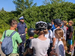 policjant ruchu drogowego przy nim zgromadzone dzieci w kaskach na głowach