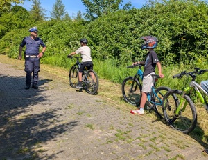 policjant ruchu drogowego przy nim  dzieci na rowerach