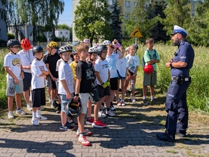 policjant ruchu drogowego przy nim zgromadzone dzieci w kaskach na głowach