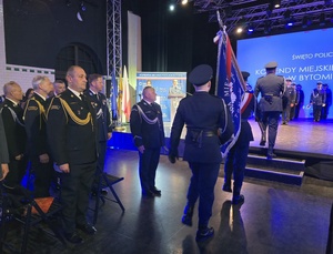 trzech policjantów maszeruje ze sztandarem pośród gości