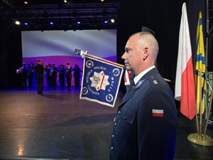 profil policjanta, obok niego scena na której gra orkiestra policyjna