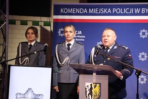 Komendant Miejski Policji w Bytomiu przemawia do mikrofonu przed mównicą obok dwie policjantki przy kolejnej mównicy