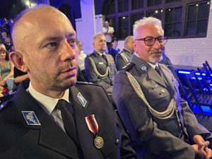 odznaczony policjant siedzi na krześle obok niego kolejny uśmiechnięty policjant