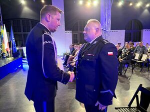 Bytomski Komendant Miejski i Pierwszy Zastępca Komendanta Wojewódzkiego Policji w Katowicach trzymają dłonie w uścisku, za nimi goście na sali