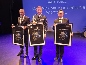 na scenie Pierwszy Zastępca Komendanta Wojewódzkiego Policji w Katowicach, Prokurator Rejonowy w Bytomiu Marek Furdzik i Prezydent Miasta Bytomia trzymają w dłoniach ramy z koszulkami