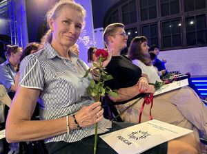 uśmiechnięta kobieta siedzi na krześle, trzyma w dłoni czerwoną różę