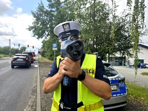policjant w trakcie pomiaru prędkości, trzyma urządzenie w dłoniach przy twarzy