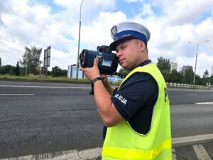 policjant w trakcie pomiaru prędkości, trzyma urządzenie w dłoniach przy twarzy