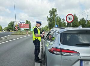 policjant w trakcie kontroli pojazdu, stoi przy oknie kierowcy pojazdu srebrnego koloru
