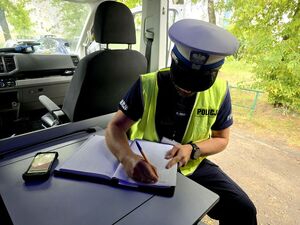 policjant w radiowozie służbowym siedzi przy stoliku i pisze w notatniku