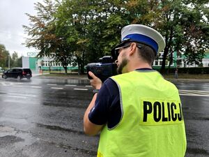 policjant przy jezdni wykonuje pomiar prędkości