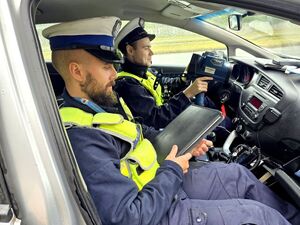 dwóch policjantów ruchu drogowego siedzących w radiowozie jeden trzyma notatnik, drugi urządzenie do pomiaru prędkości