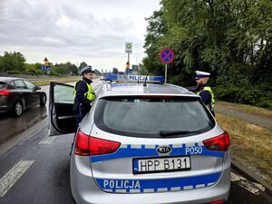 policjanci po obu stronach radiowozu, wchodzą do niego