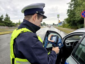 policjant stojący przy radiowozie sprawdza pomiar, patrzy na urządzenie do pomiaru prędkości trzymane w dłoniach