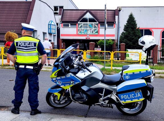 policjant przy motocyklu służbowym stojący przed szkołą