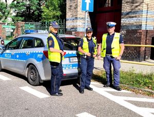 policjant i dwie strażniczki miejskie stojący przed szkołą