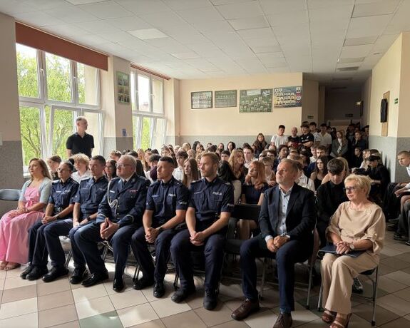 policjanci i zgromadzone osoby siedzący na krzesłach w sali