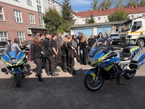 policjantka, dwa motocykle policyjne i licealiści zgromadzeni na parkingu